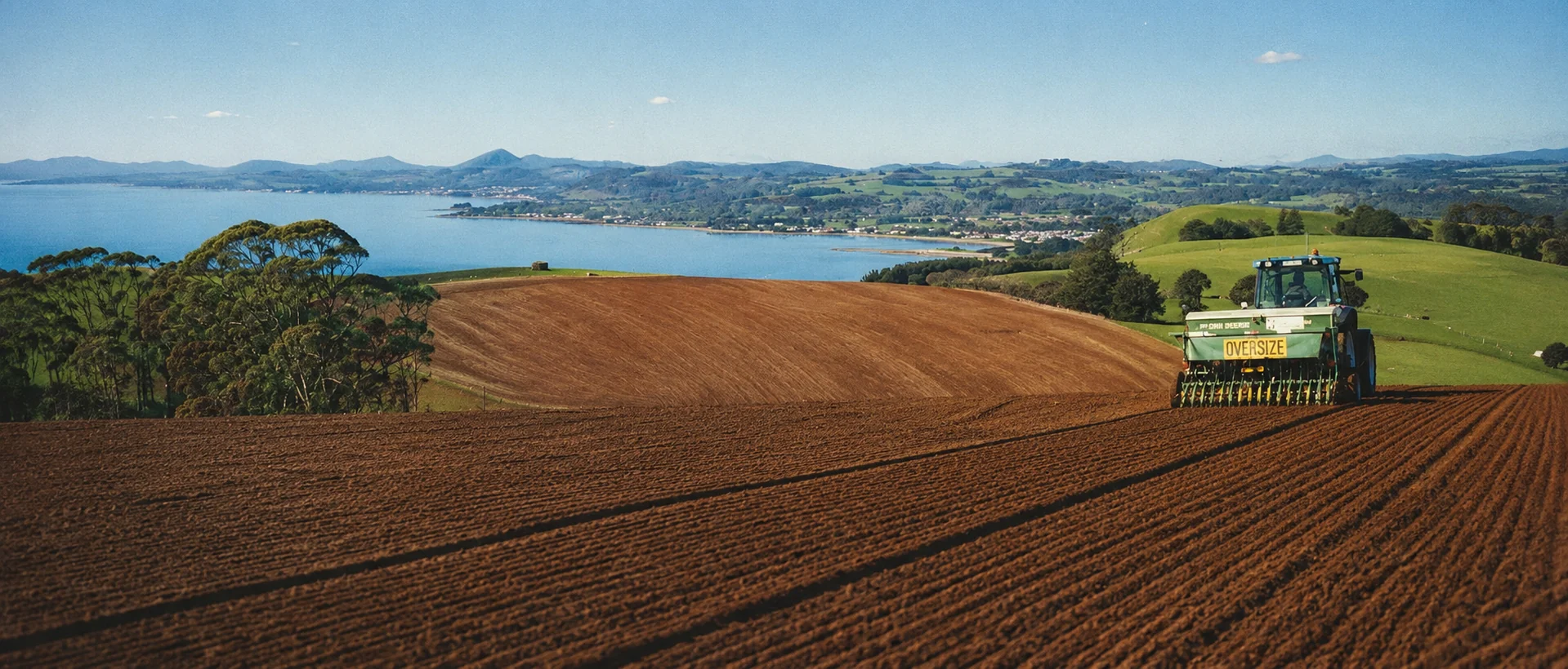 Tractor working in a cultivated field overlooking the Tasmanian coastline